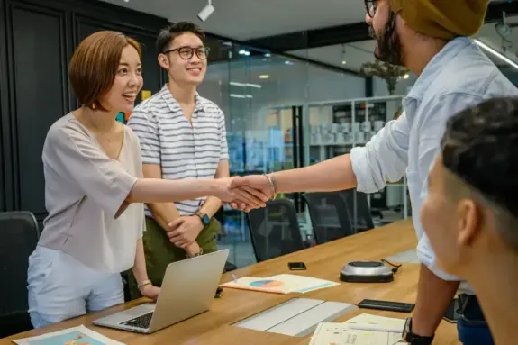 Buyer and seller shaking hands across a meeting table after agreeing a deal