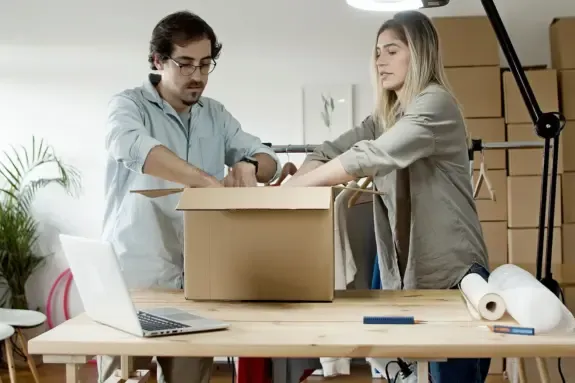 Two business partners packing product orders into a cardboard box at a work table