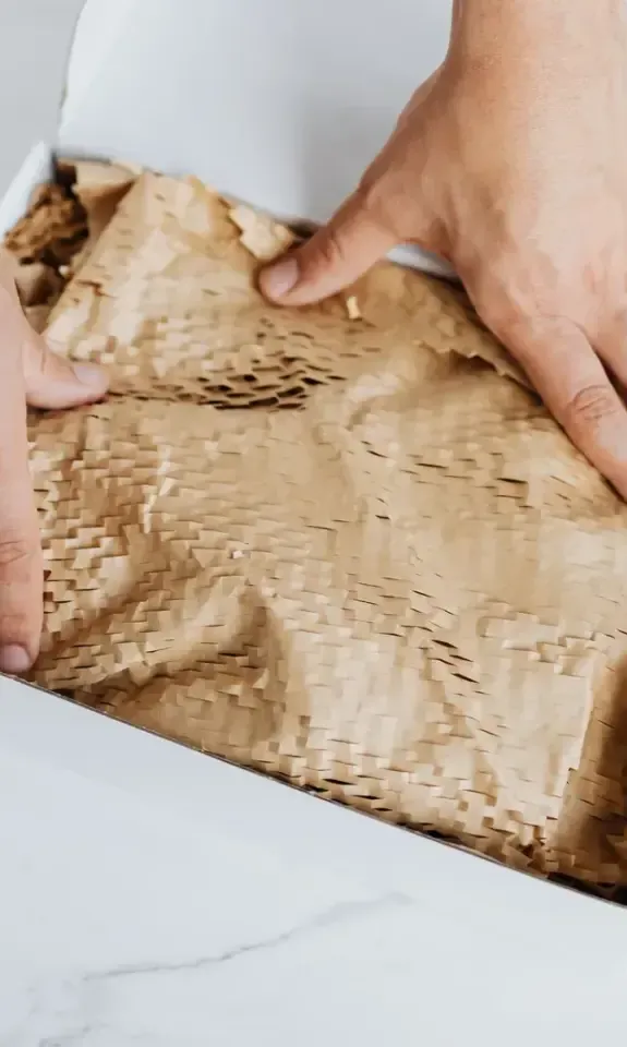 Hands packing a cardboard shipping box with protective paper