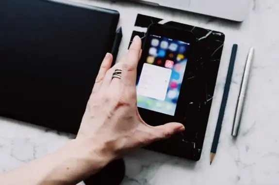 Hand using mobile apps on a smartphone resting on a marble desk