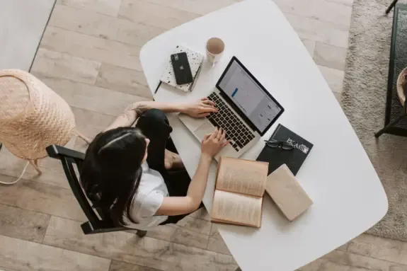 Overhead view of a writer typing on a laptop at a home desk with notebooks
