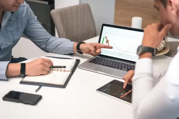 Two business people reviewing financial charts on a laptop and tablet during a meeting