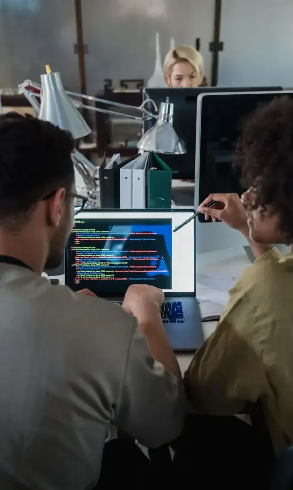 Two software developers reviewing code on a laptop, the kind of product work buyers examine when founders sell a SaaS business